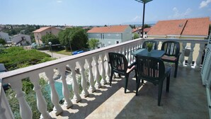 Varanda com mesa e cadeiras, vista para uma área residencial com casas e uma piscina.