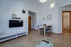Un salon moderne doté d’un téléviseur à écran plat, d’une table basse en verre et d’un coin repas avec une table et des chaises en bois.