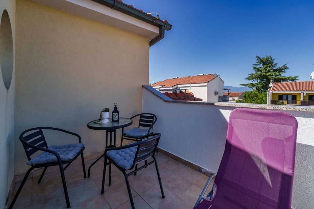 Un balcon avec une table et deux chaises, dont une chaise violette, et une vue sur les bâtiments voisins.