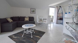 Ein modernes Wohnzimmer mit einem dunkelgrauen Sofa, einem weißen Esstisch mit Stühlen und einem einzigartigen weißen Couchtisch mit runder Basis.