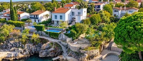 A coastal residential area with houses, a clear blue pool, and a stone bridge.