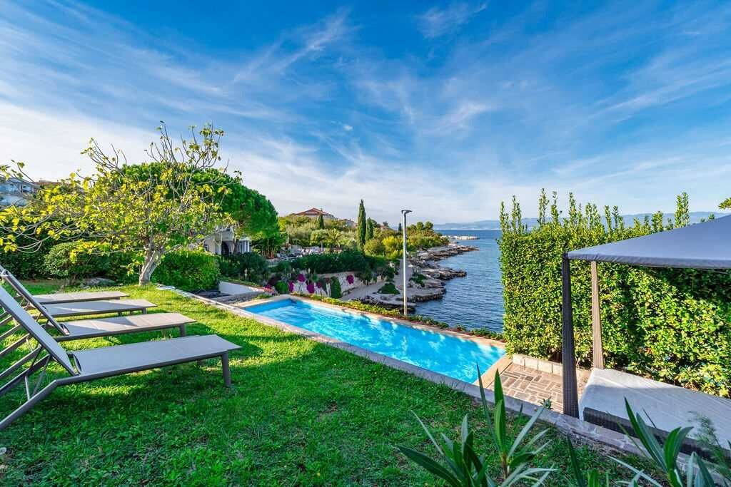 Une piscine avec des chaises longues, une vue sur la mer et un jardin bien entretenu.