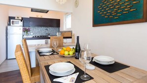 Une cuisine moderne avec des meubles de couleur sombre, un four à micro-ondes et un plan de travail recouvert de carreaux. Une table à manger est dressée, avec des assiettes, des verres et une bouteille de vin.