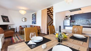 Un salon moderne avec un coin repas, comprenant une table à manger en bois pour deux personnes, un canapé et une cuisine en arrière-plan.