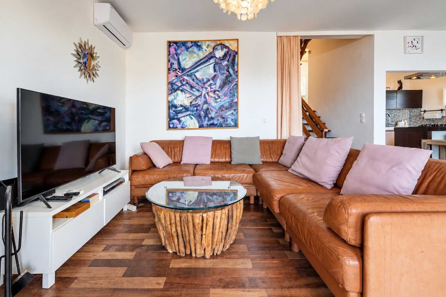 A modern living room with a leather sofa, a glass coffee table, and a large abstract painting.