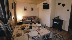 Un comedor acogedor con una mesa lista para dos personas, un sofá y un televisor montado en la pared.