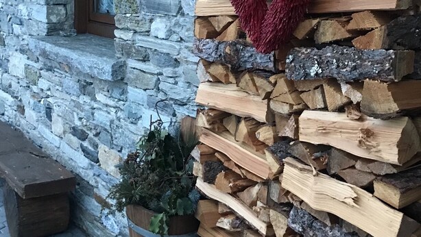 Un edificio de piedra con un muro de madera apilada de leña y una decoración con forma de corazón rojo.