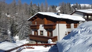 Una cabaña de madera con balcón, rodeada de árboles cubiertos de nieve y un cielo despejado.