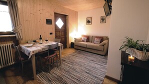 Una habitación acogedora con techo de madera, una mesa de comedor para dos personas, un sofá y una planta pequeña sobre una mesita.