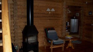 Accogliente interno di una baita in legno, con un camino a legna, un'area pranzo con tavolo e sedie, e un frigorifero sullo sfondo.