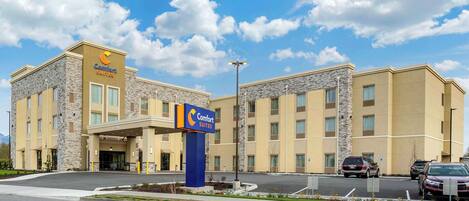 A Comfort Suites hotel with a stone facade, a blue entrance sign, and a parking lot with several cars.