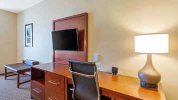 Habitación de hotel con un escritorio de madera, una silla, un televisor montado en la pared y una lámpara de noche.
