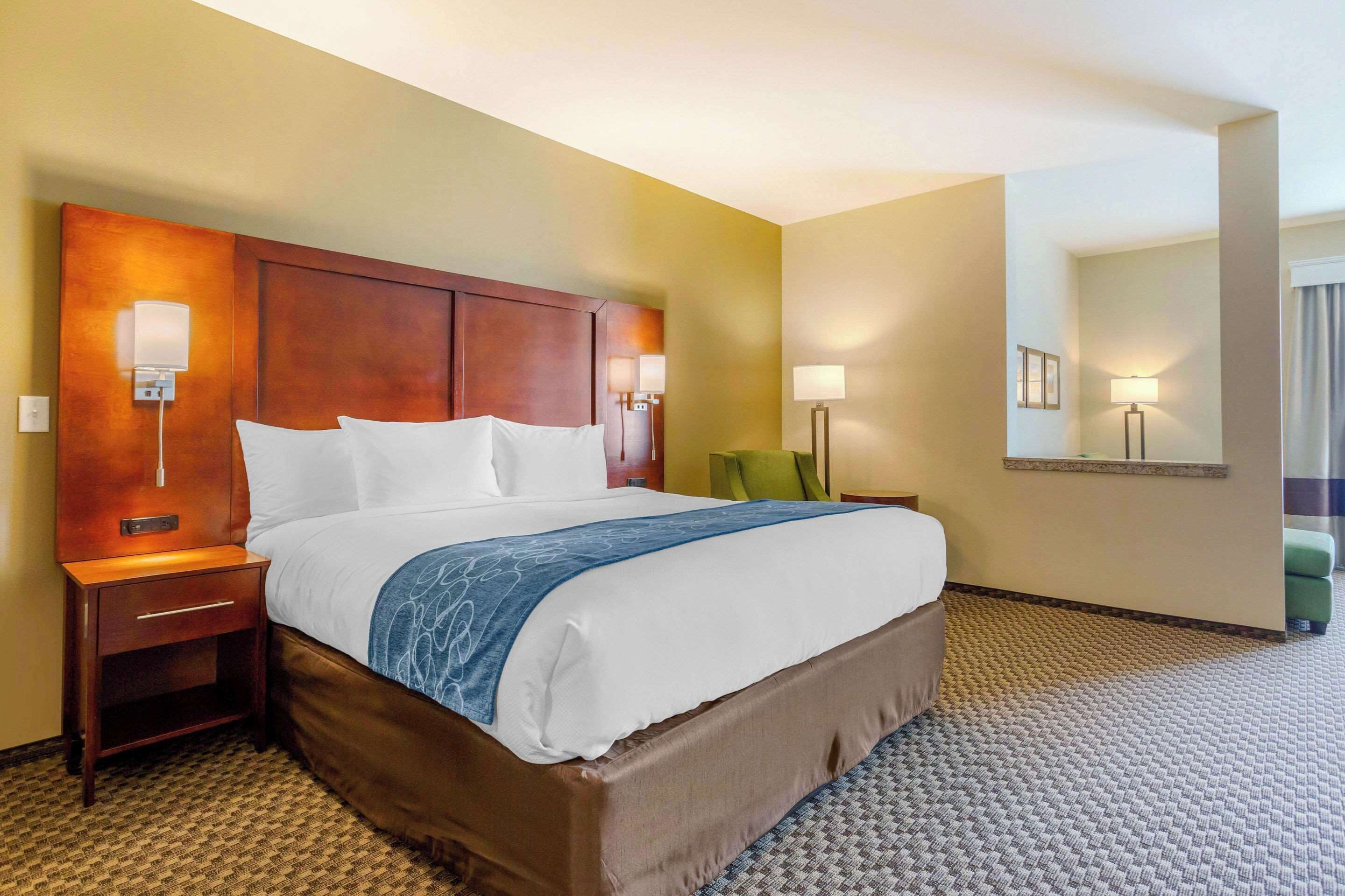 Habitación de hotel con una cama grande, lámparas de noche, mesita de noche, una silla verde y un espejo en la pared.