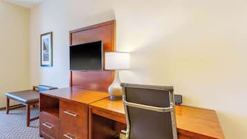 A hotel room with a wooden desk, a chair, a flat-screen TV, a lamp, and a framed picture on the wall.