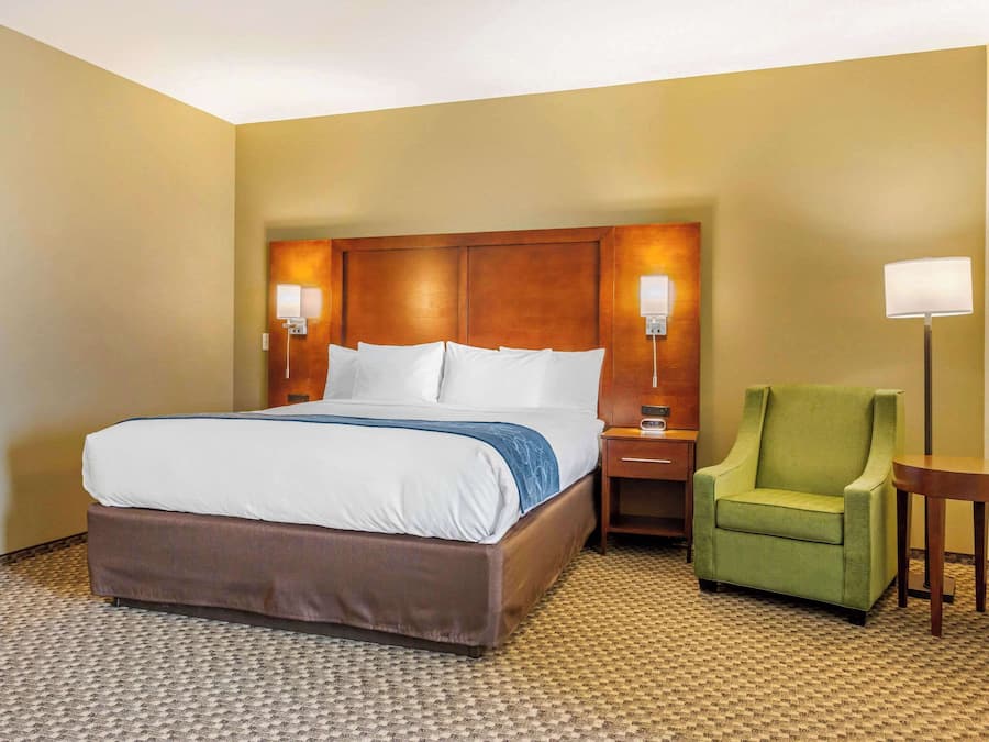 Ein Hotelzimmer mit einem großen Bett, einem grünen Sessel, einem Nachttisch und einer Lampe.