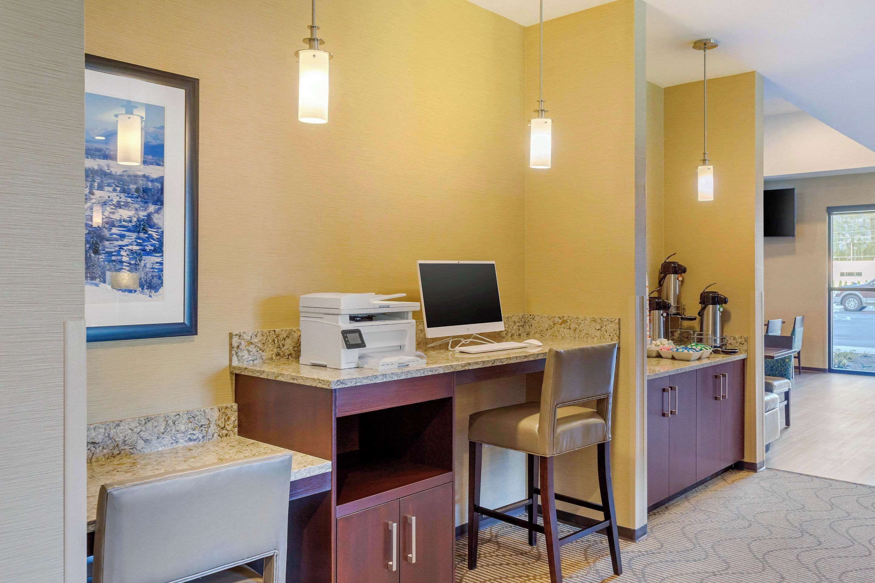 A hotel room with a desk, chair, and a coffee machine. There is a framed picture on the wall and a television mounted on the wall.