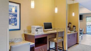 A hotel room with a desk, chair, and a coffee machine. There is a framed picture on the wall and a television mounted on the wall.