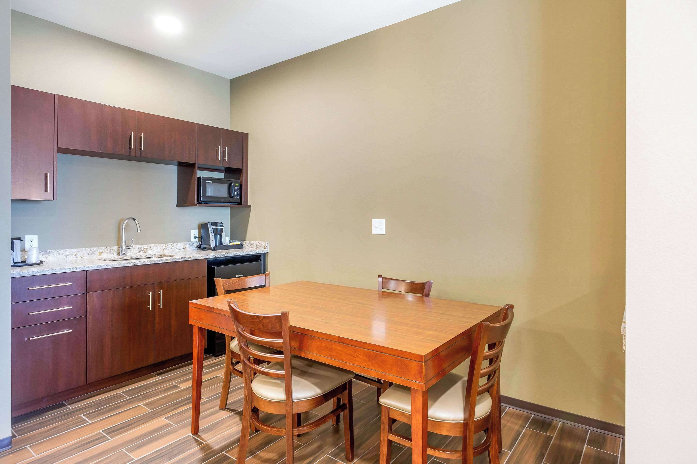 Cocina compacta con armarios de madera, microondas y una mesa de comedor con sillas.