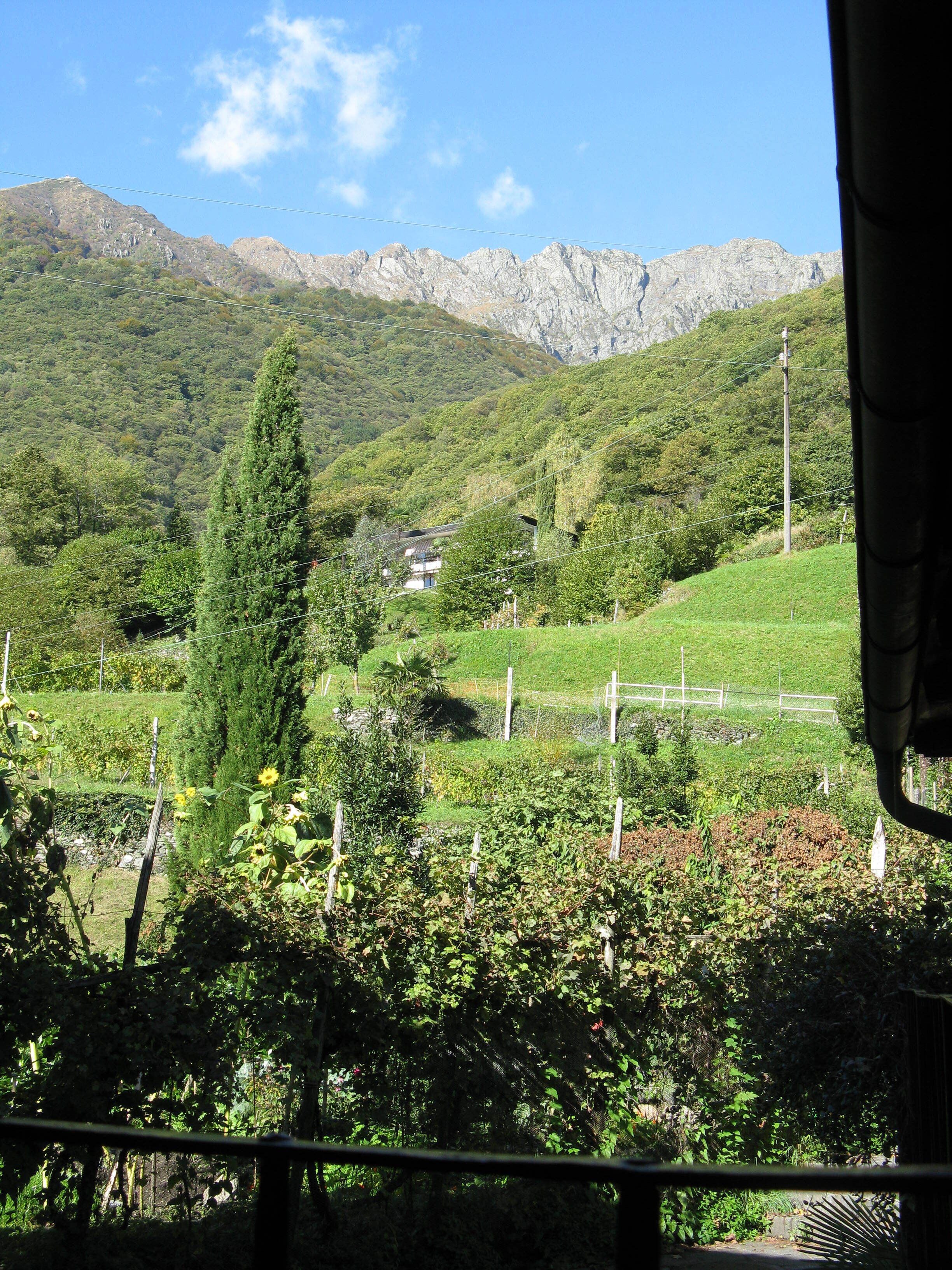 A mountainous landscape with a house nestled among greenery, a clear sky, and power lines.