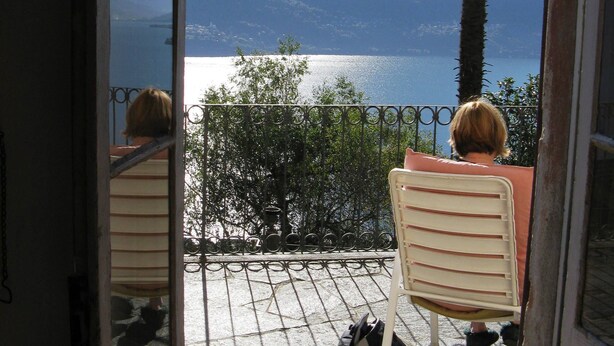 Un balcon avec vue sur un lac et des montagnes, un palmier et une chaise.