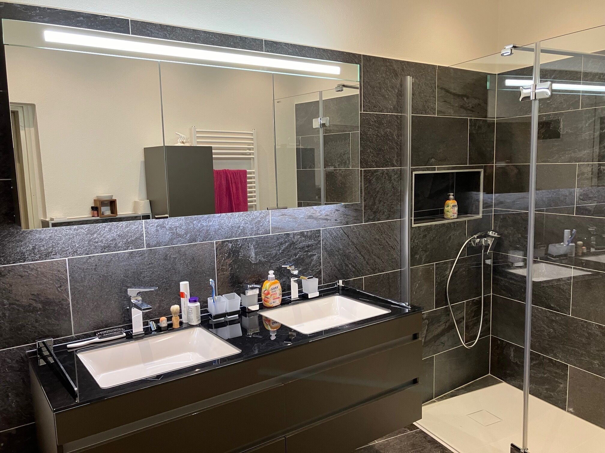 Une salle de bain moderne avec deux lavabos, un grand miroir et une douche séparée par une paroi de verre.