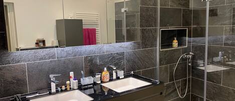 Une salle de bain moderne avec deux lavabos, un grand miroir et une douche séparée par une paroi de verre.