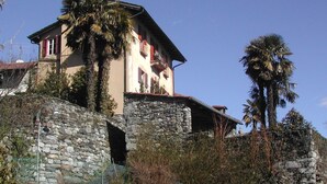 Une maison en pierre dotée d’un balcon, entourée de verdure et sous un ciel dégagé.