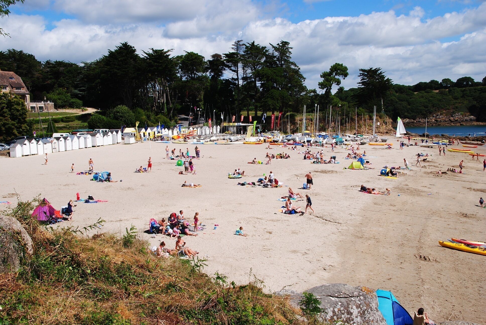 Une plage où l’on peut voir des gens se prélasser au soleil et se baigner, ainsi que des tentes et des bateaux.