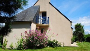 Ein modernes Haus mit Balkon, umgeben von einem gepflegten Garten mit rosa Blumen.