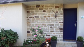 Ein Steinhaus mit einer blauen Tür, ein Hund sitzt im Gras, und es stehen Blumentöpfe herum.