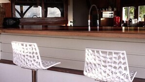 Zona de bar con dos sillas blancas, una barra de madera y un ventanal con vistas.