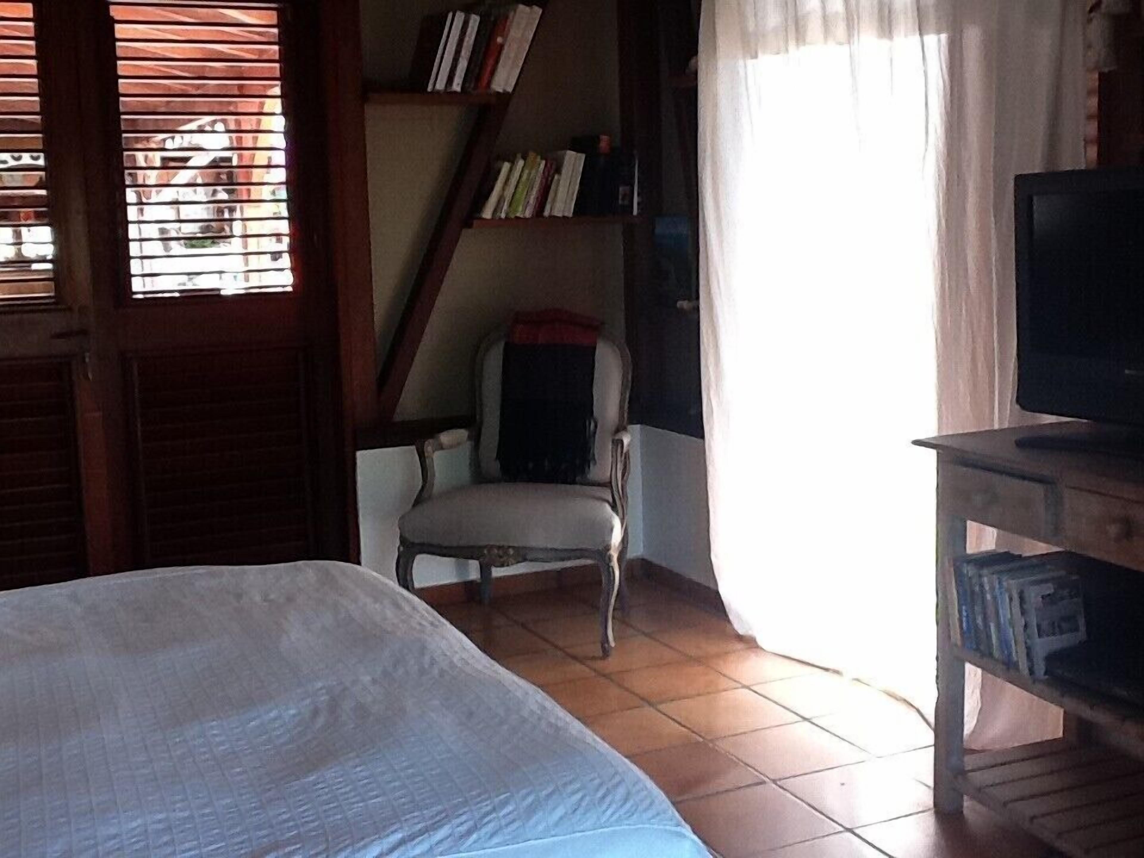 Een slaapkamer met een bed, een stoel, een televisie en een boekenkast.