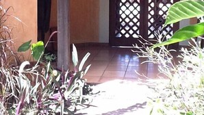 Una entrada cubierta con una puerta celosíaca, rodeada de follaje y un suelo de baldosas.