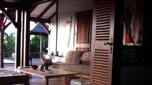 Un espacio al aire libre techado con un banco de madera, una mesa y un sofá.