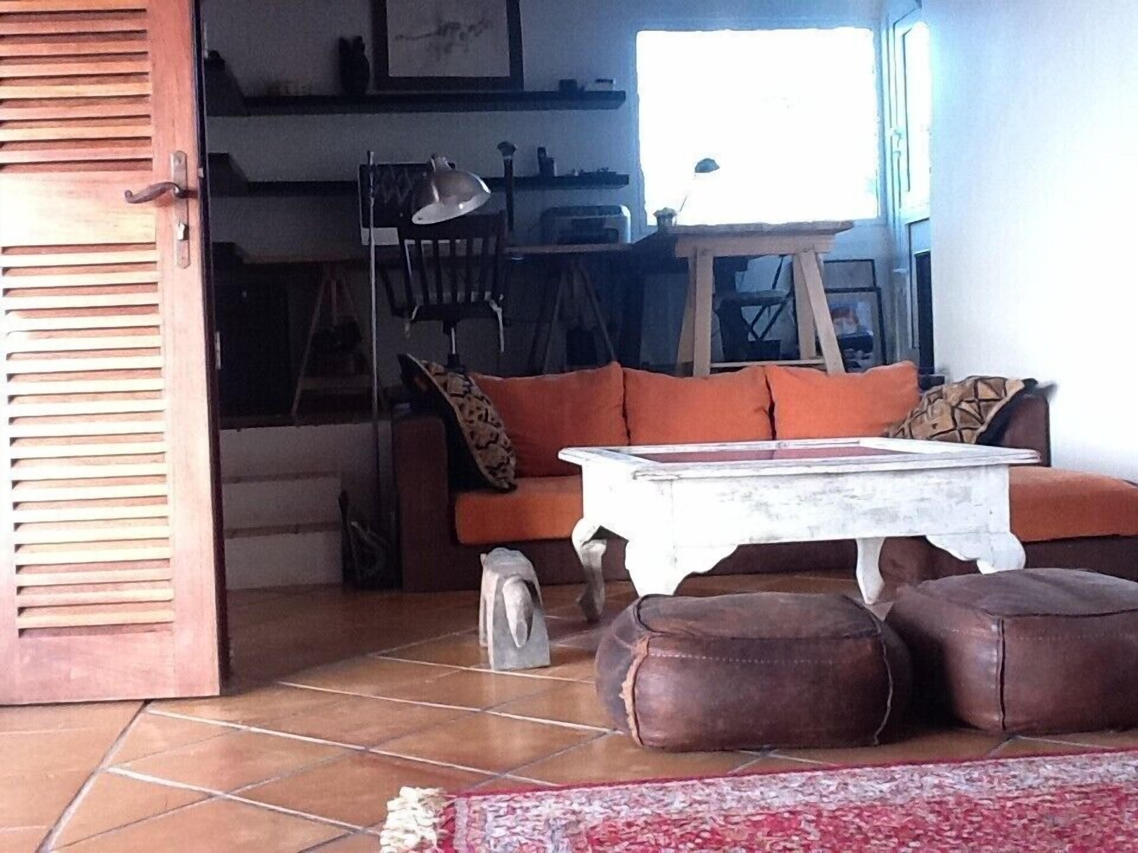 Ein Wohnzimmer mit einer Couch, Poufs, einem Couchtisch und einem Essbereich im Hintergrund.