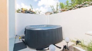 A hot tub in a backyard with a white wall, a small garden, and a clear sky. - Studio with private jacuzzi (Sainte-Anne)