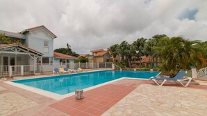 A swimming pool with lounge chairs, a stone-tiled deck, and a building with a red-tiled roof. - Studio with private jacuzzi (Sainte-Anne)