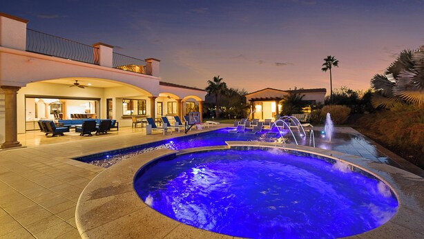 Piscina com iluminação azul, espreguiçadeiras e área de estar com restaurante.