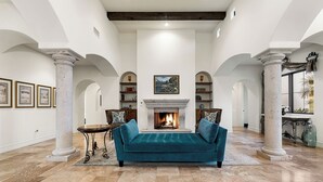 A spacious living room with a fireplace, a sofa, and bookshelves. - 6,000 SQFT Luxurious Mansion w/Heated Pool, Spa, Pickleball & Mountain Views (Paradise Valley)