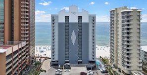 Un hôtel doté d’une tour centrale portant l’inscription « Island Royal », entouré d’autres bâtiments, d’un parking et d’une plage agrémentée de parasols.