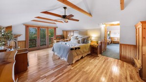 Un dormitorio espacioso con vigas de madera, una cama grande, un ventilador de techo y vistas a través de un gran ventanal corredizo.