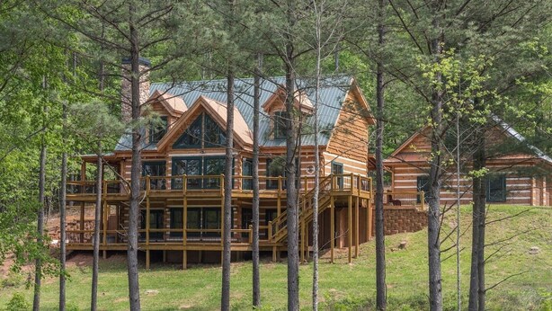Uma cabana de toras com varanda em vários níveis, cercada por árvores.
