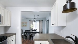 Una cocina moderna con armarios blancos, una isla central y un comedor visible a través de un arco.