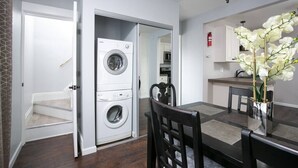 Una cocina moderna con lavadora y secadora integradas, un comedor con mesa y sillas, y un jarrón decorativo con orquídeas.