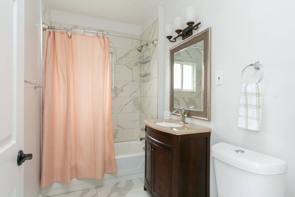 Un baño con cortina de ducha, bañera, tocador con lavabo, espejo y retrete.