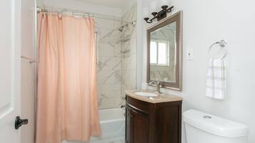 Un baño con cortina de ducha, bañera, tocador con lavabo, espejo y retrete.