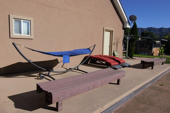A patio with a hammock, two lounge chairs, and a bench.