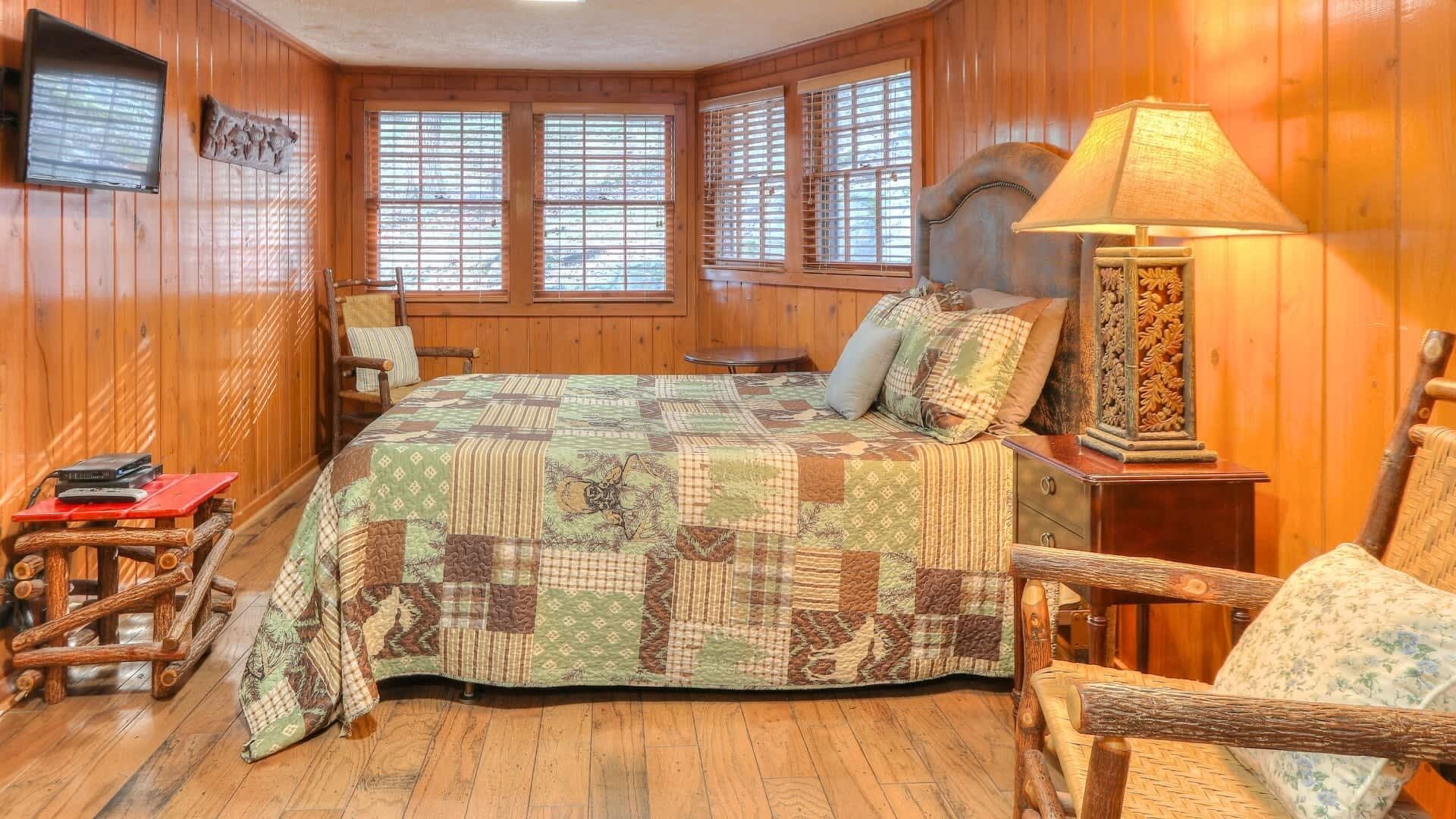 A wooden-paneled room with a bed, a chair, a lamp, and a small table.