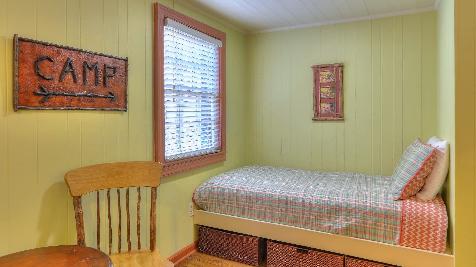 Una habitación con cama, una silla, una ventana con persianas y un letrero en la pared.