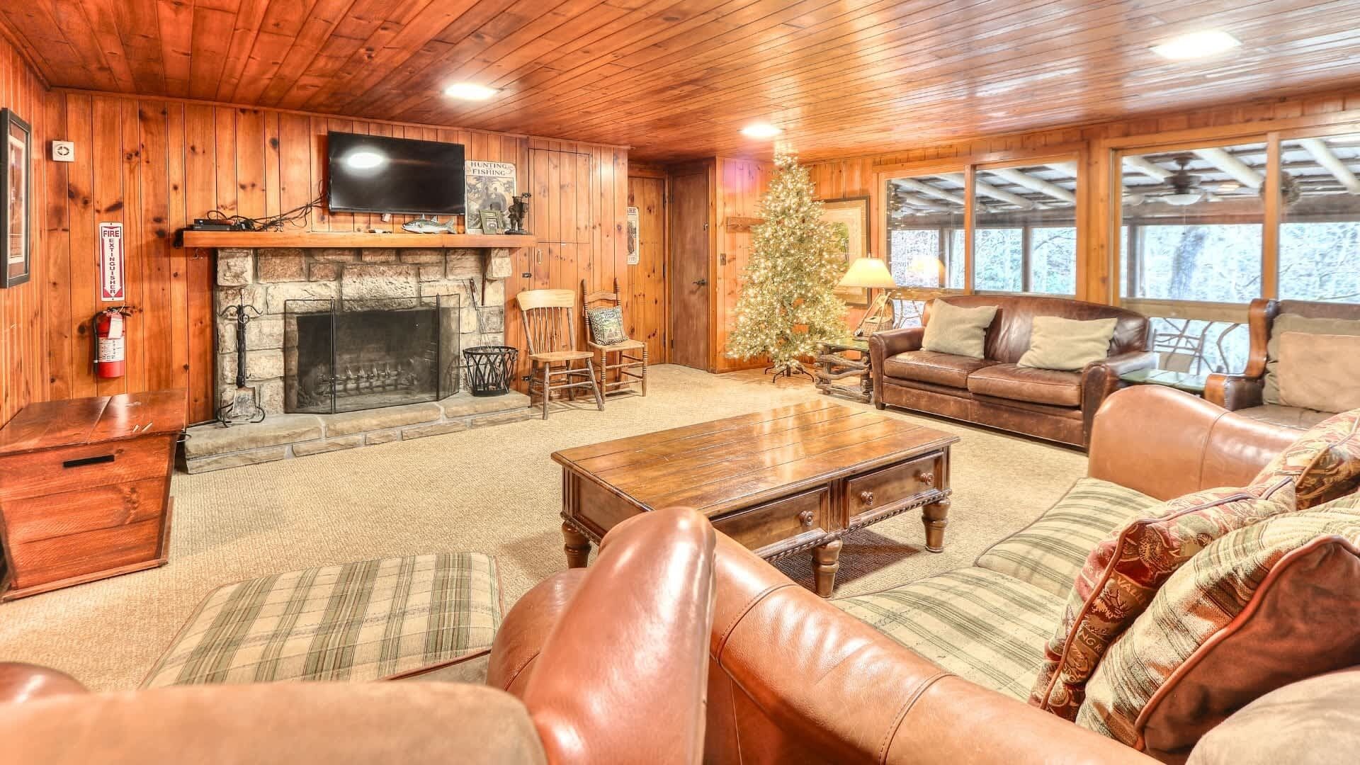 L’intérieur chaleureux d’un chalet avec une cheminée en pierre, des meubles en cuir, un sapin de Noël et un téléviseur fixé au-dessus de la cheminée.
